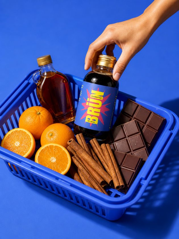 Hand lifting a BRÜN bottle from a blue crate with oranges, chocolate and cinnamon