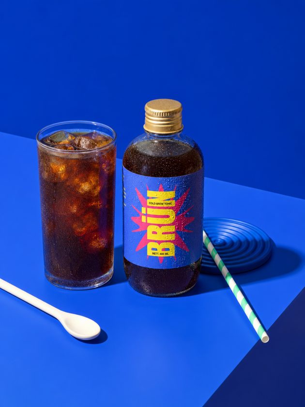 BRÜN bottle next to a glass of iced cold brew on a blue table