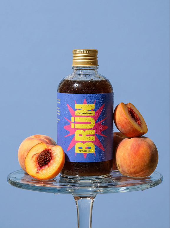 BRÜN Cold Brew Tonic bottle with peaches on a glass stand